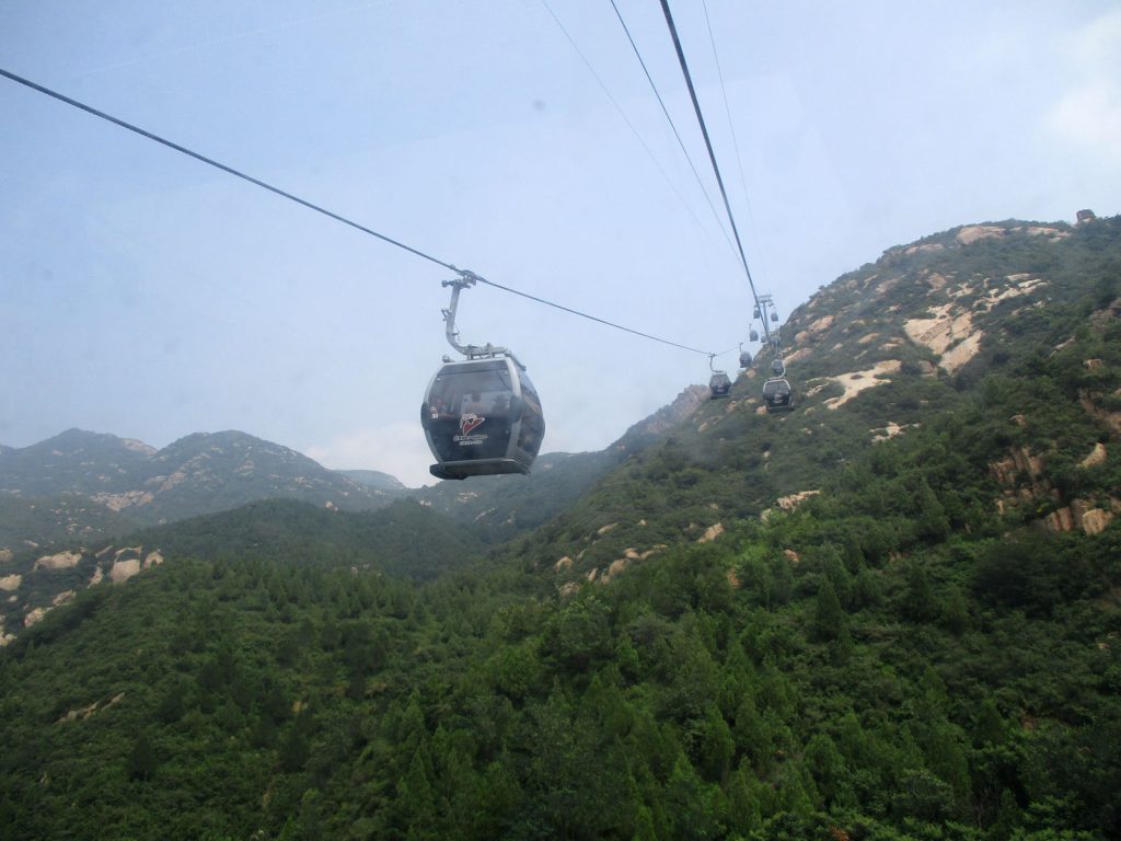 Cableway cabins travelling over green hills near Badaling Great Wall